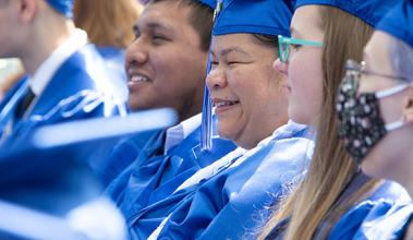 Several students smile in blue graduation robes while seated at graduation