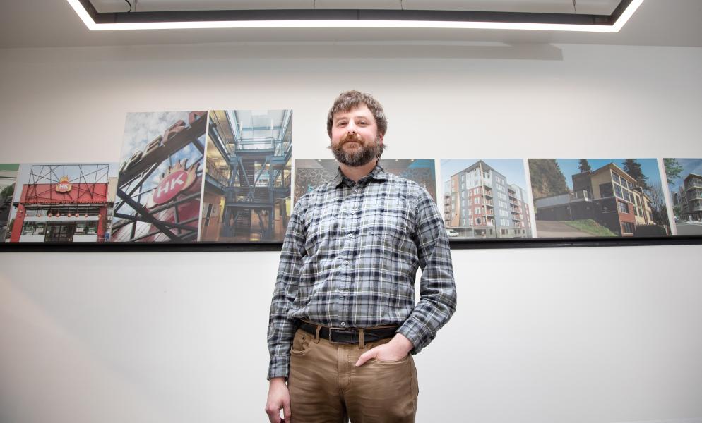 Alumni Justin Losey standing in front of a white wall with photos of buildings