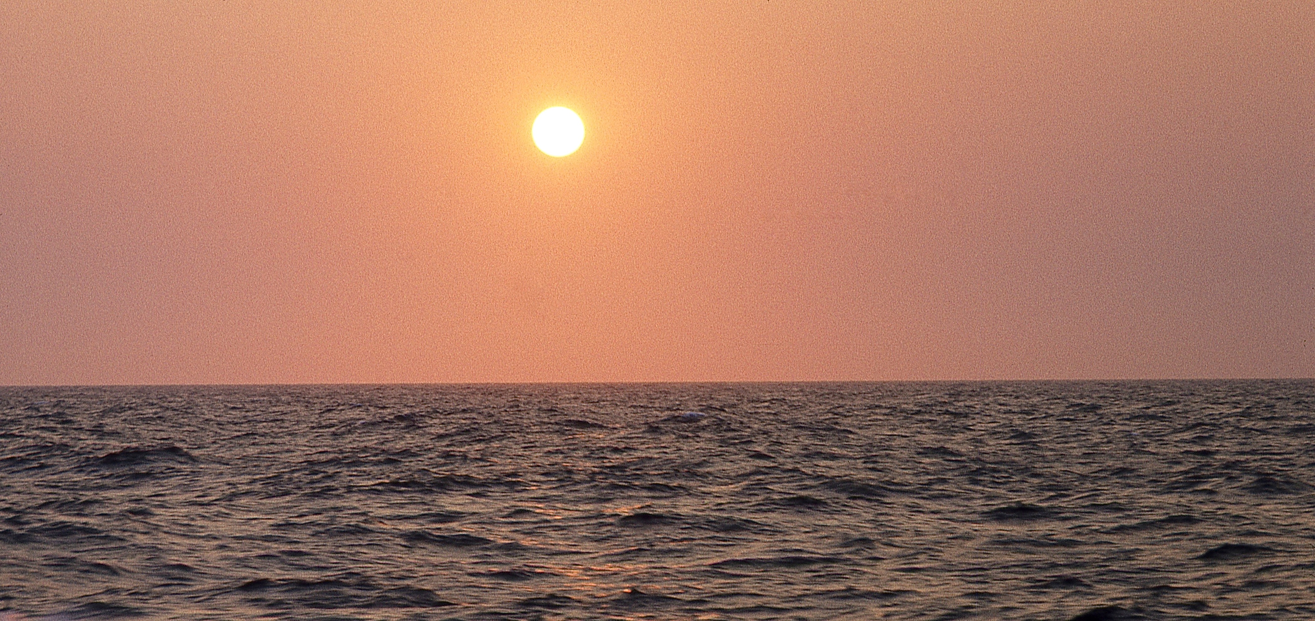 A photograph of the sun in a red sky over the horizon and water below