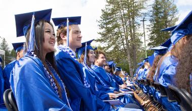 Students smile in blue caps and gowns at graduation ceremony
