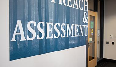 A white wall with text that reads "Outreach & Assessment"