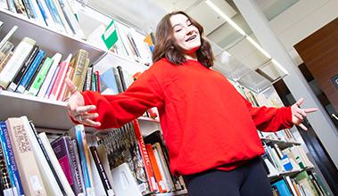 Student in a red sweater standing in front of a bookshelf in the library