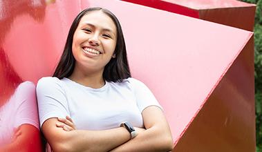 Student smiles with arms crossed in front of red sculpture