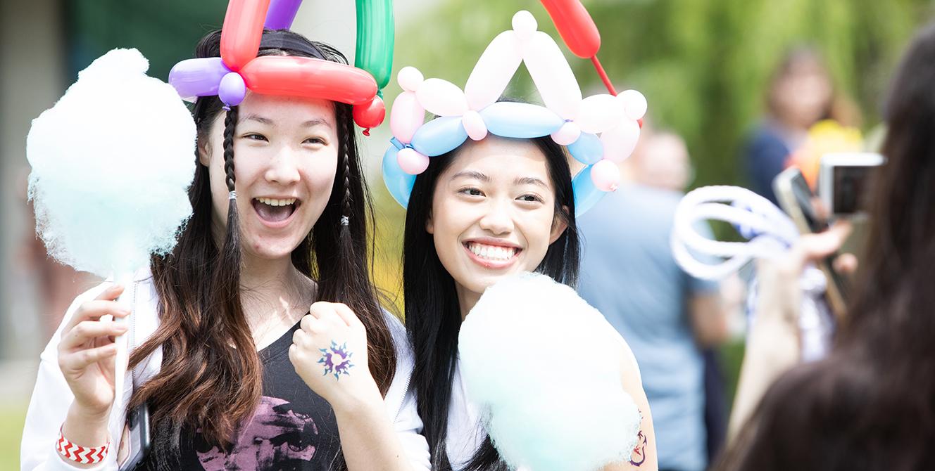 Two students wearing balloon crowns and holding cotton candy on paper cones