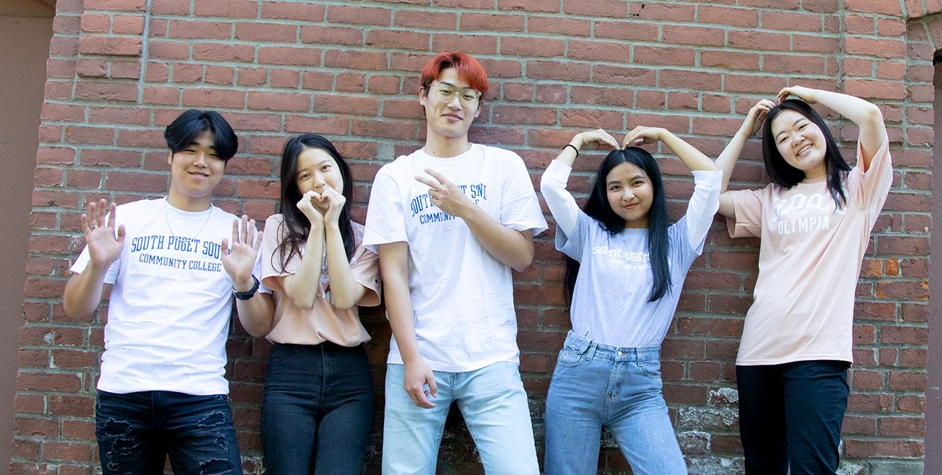 five students pose in front of a brick wall