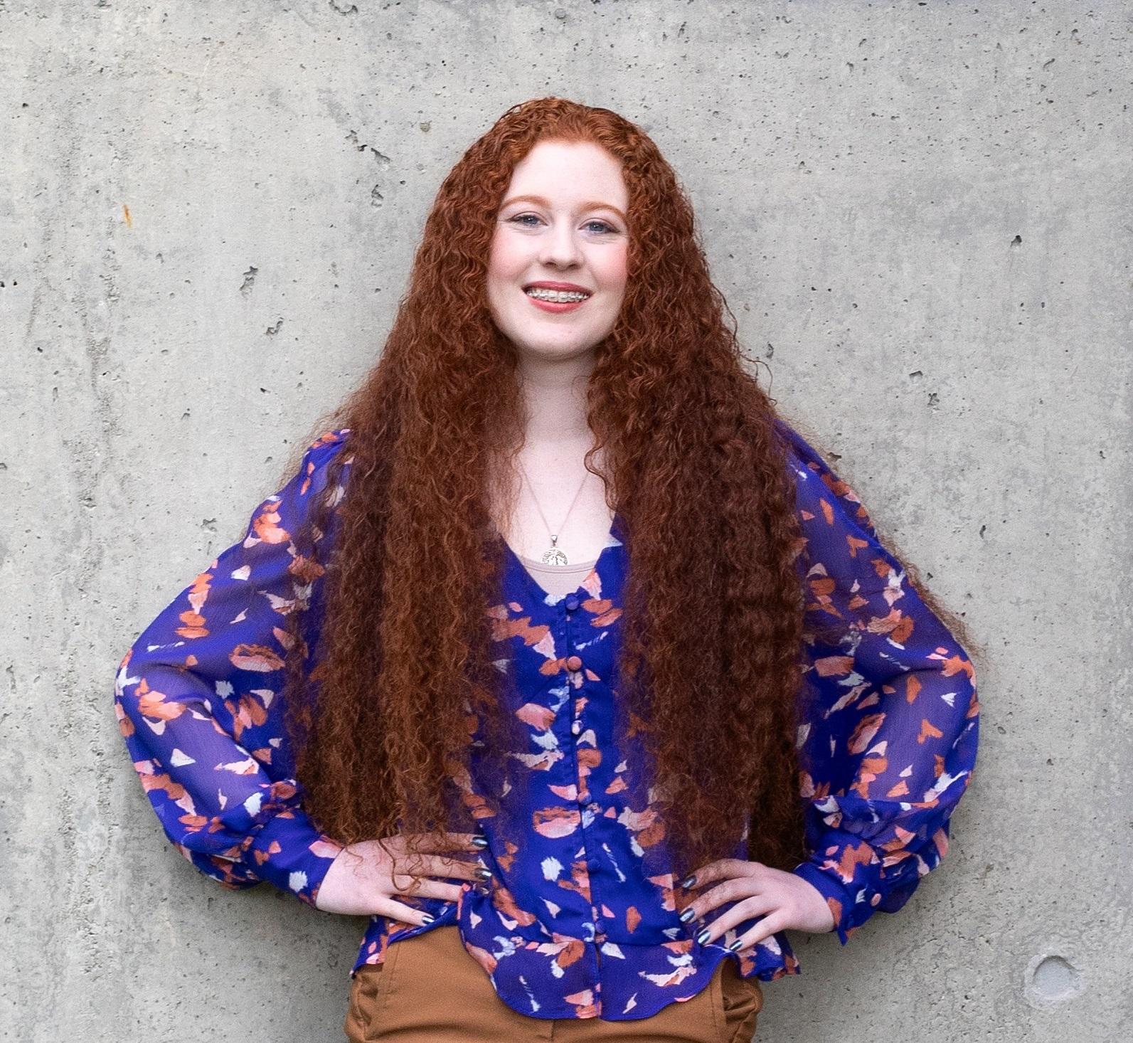 Student with long red curls smiles in purple blouse