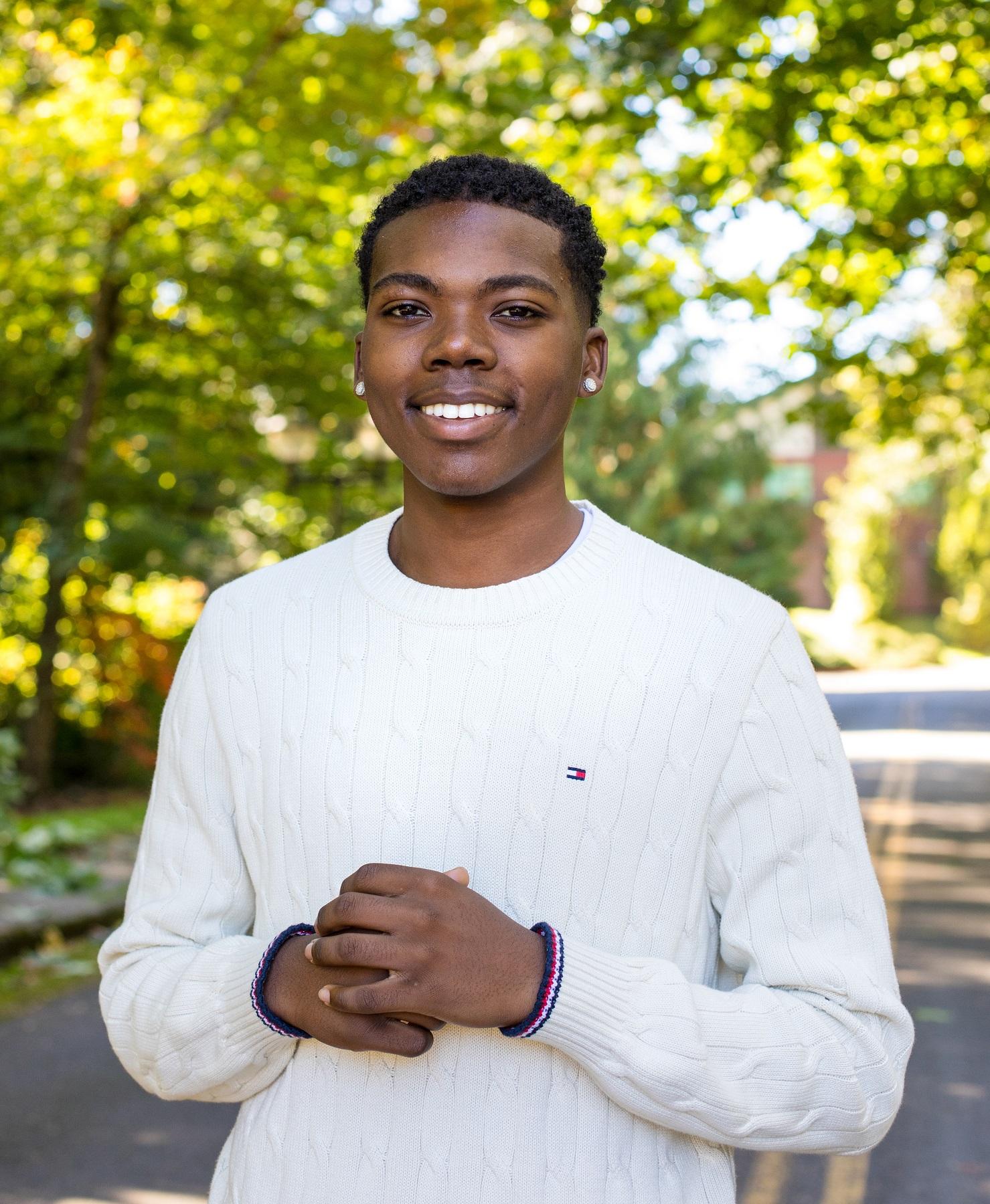 Student in white sweater stands in front of trees