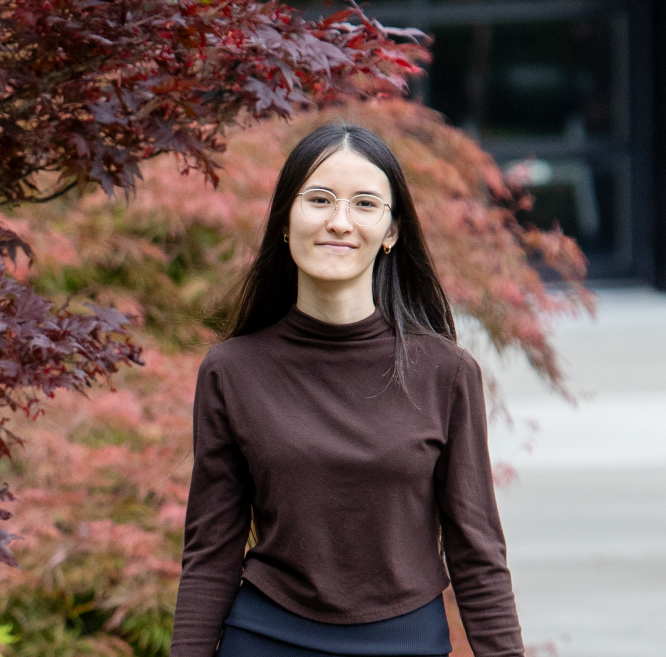 Student in glasses smiles at camera in front of maple leaves