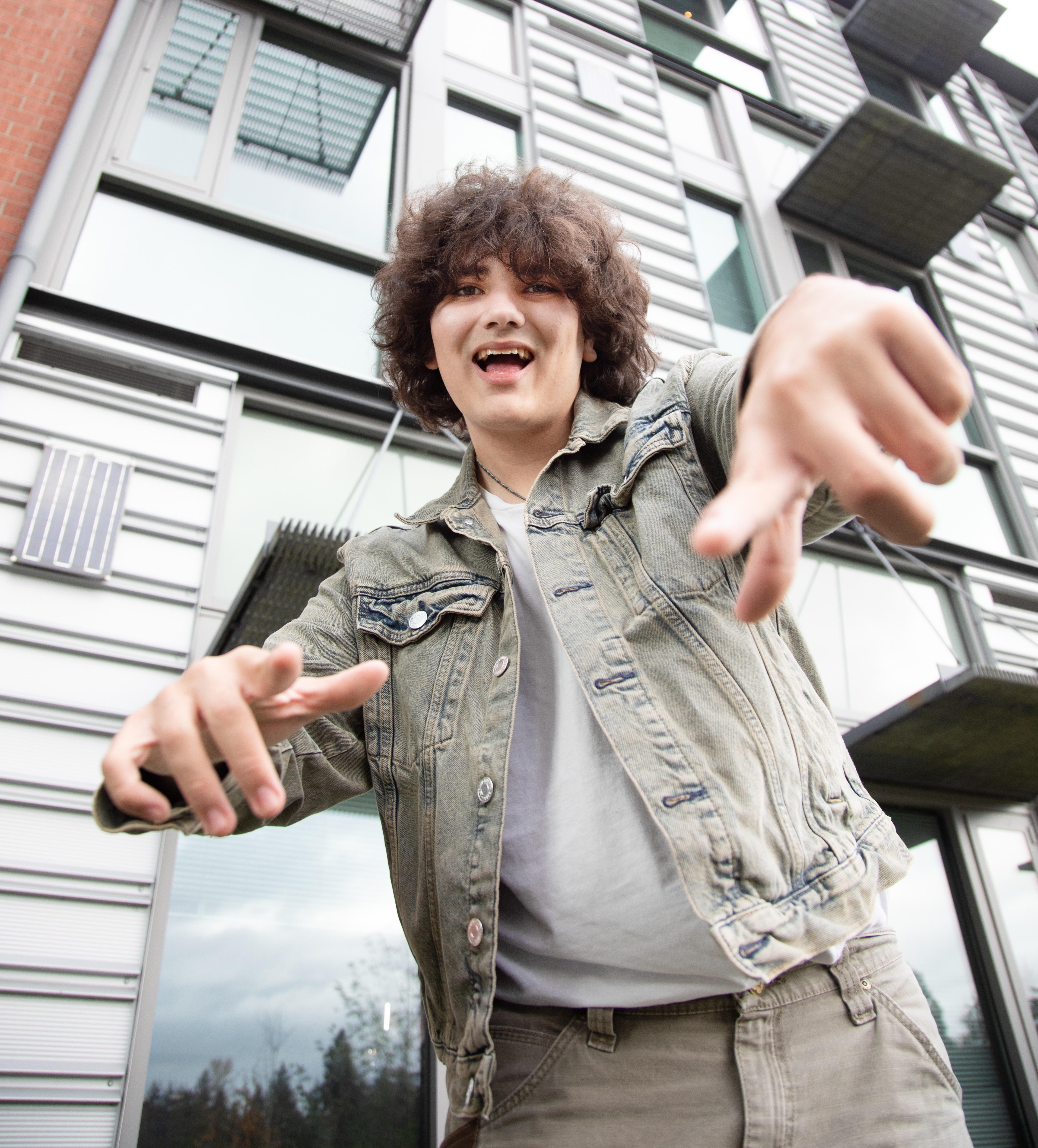 Student smiles and points at camera in front of modern building