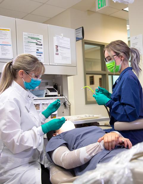 An instructor and student working on a patient in a dental clinic