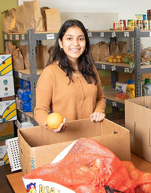 Student unpacking an orange from a box with shelves of food behind them