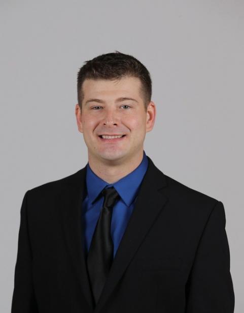 Maxwell Sampson, Head Coach of Clipper Men's Soccer, wearing a black suit and tie with a blue button up