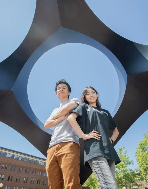 Two students standing beneath a sculpture pointed up at the sky on Western Washington University's campus