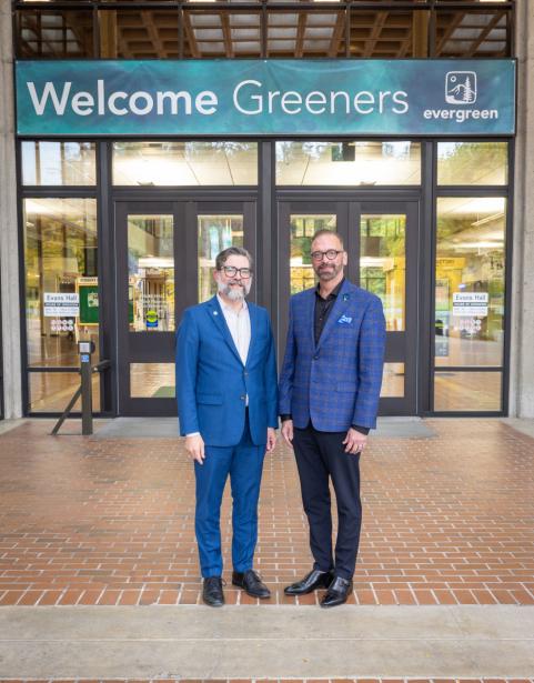 Dr. John Carmichael and Dr. Timothy Stokes in front of a sign that says "Welcome Greeners" on The Evergreen State College campus
