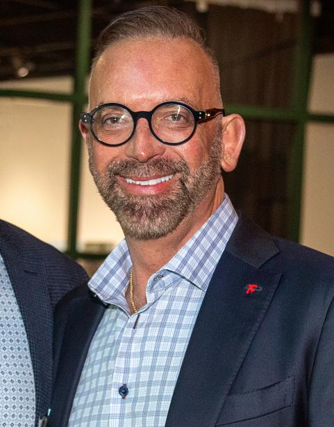 President Tim Stokes smiles with round black frame glasses and a blue suit jacket