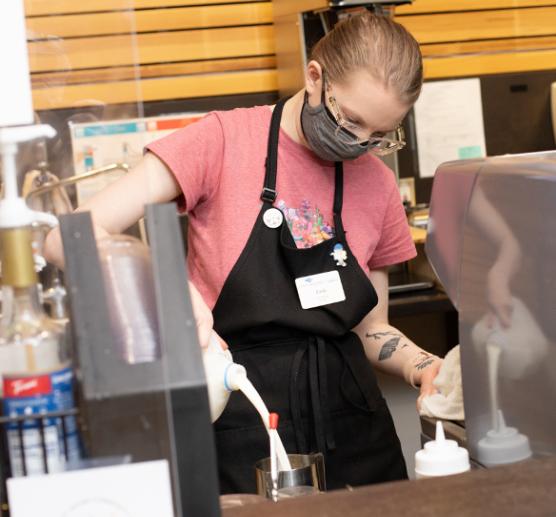 Barista pouring milk into a cup behind the counter of a cafe
