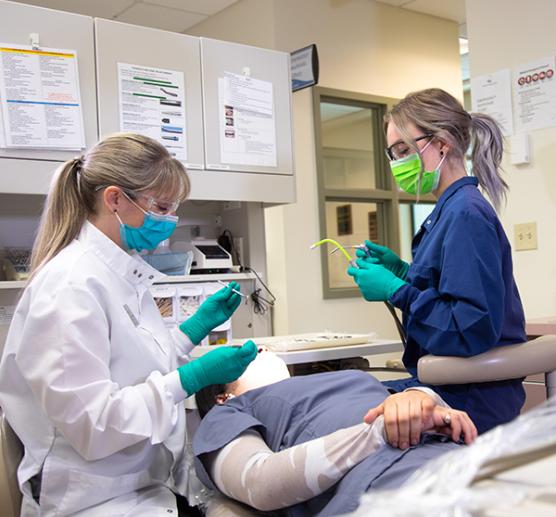 An instructor and student working on a patient in a dental clinic