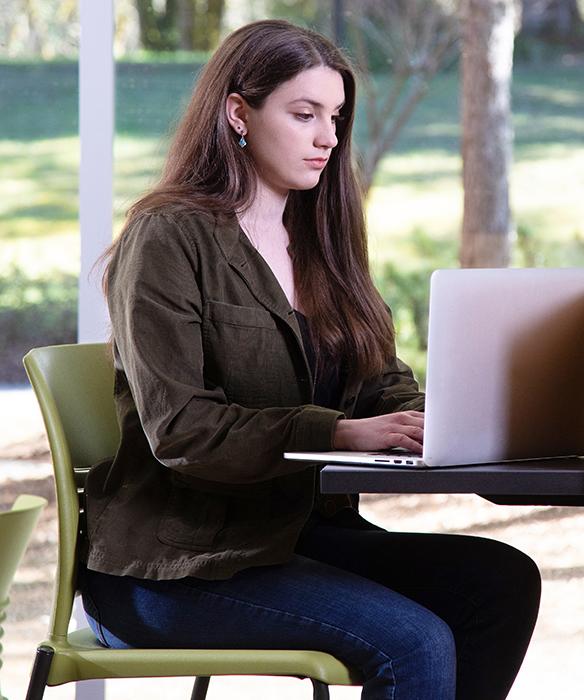 Student sits in green chair typing on laptop