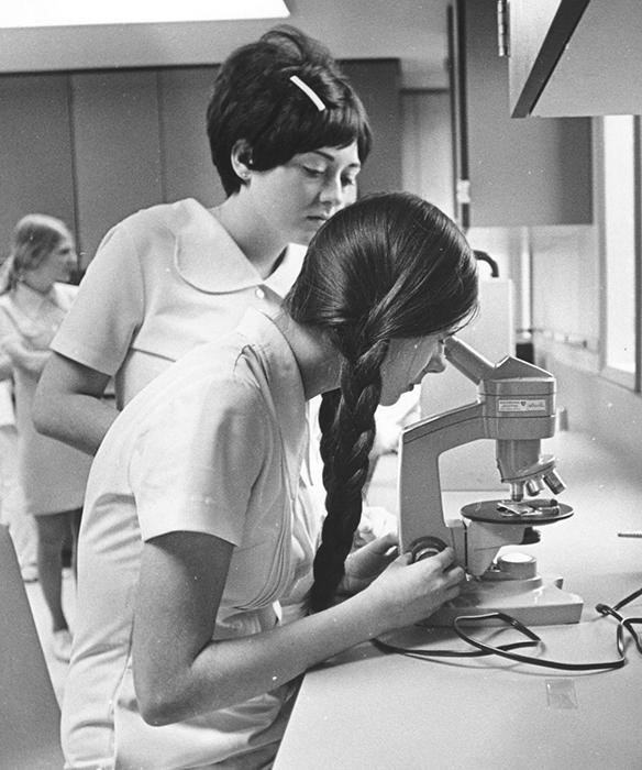 Two people looking into microscope in black and white 