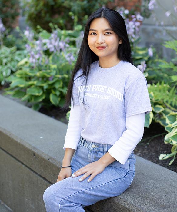 Asian student in SPSCC tshirt smiles while sitting next to plants outside