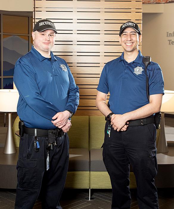 Two security officers smiling in front of a wood wall