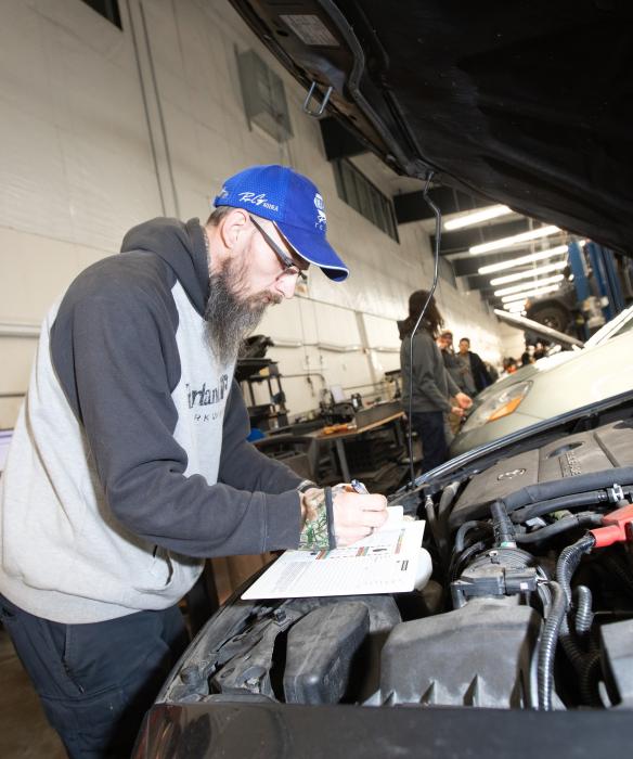 Student looks under hood of a vehicle in auto shop