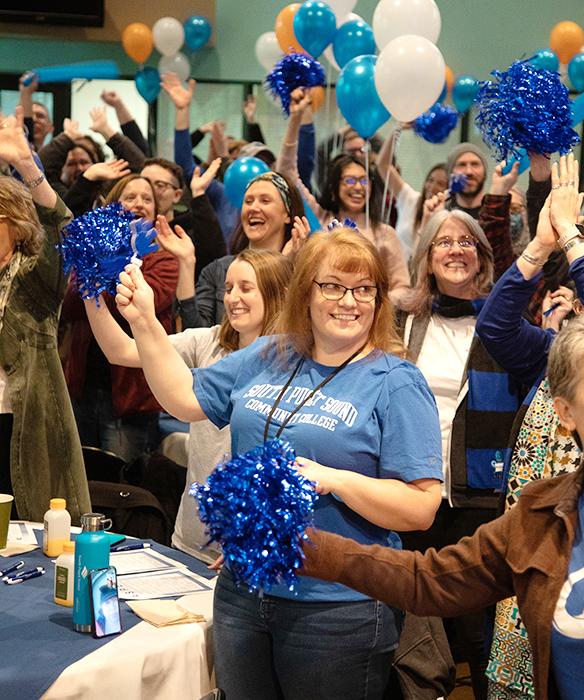 Staff smiling at a celebration with blue balloons and pom poms