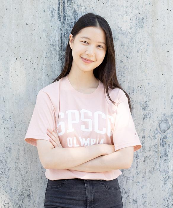 Student smiles, looking at camera, with arms crossed, wearing a light pink SPSCC t-shirt