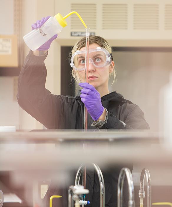 Student wtih gloves and goggles handles science equipment in lab