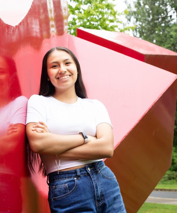 Student smiles with arms crossed, leaning on a large red statue