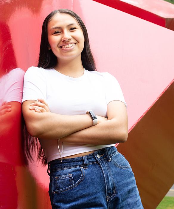Student smiles with arms crossed in front of large red scultputure