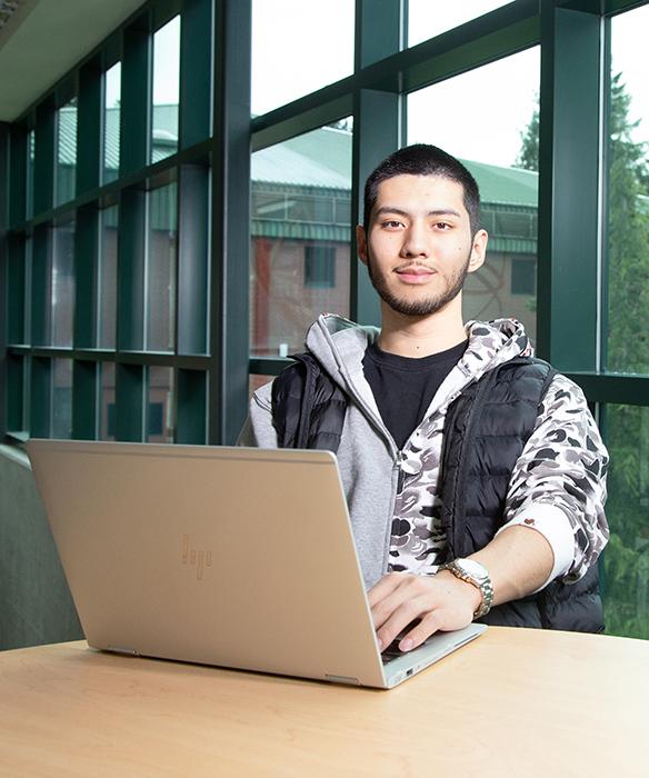 Student sits with laptop in front glass window wall