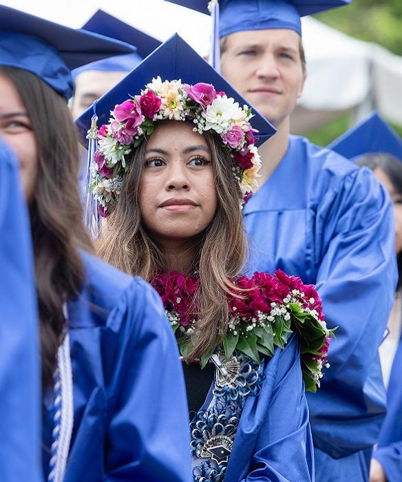 Student at graduation wearing a flower lei and flowers on graduation cap