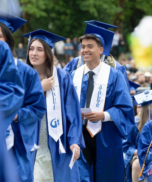 Two student athletes smiling in blue cap & gown at graduation