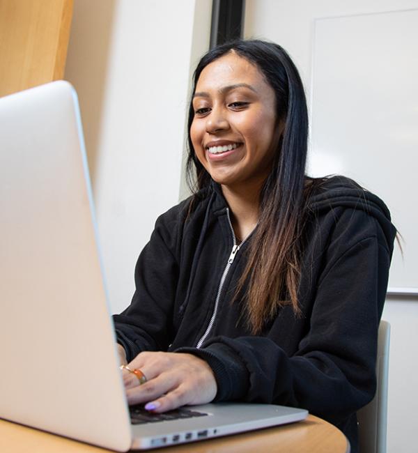 Student at laptop typing and smiling