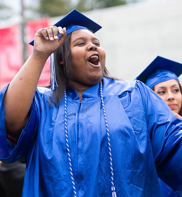 Student in blue graduation gown appears to cheer in celebration
