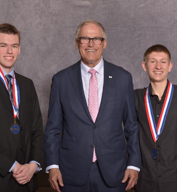 WA Gov. Jay Inslee smiles with two students wearing medallions around their neck