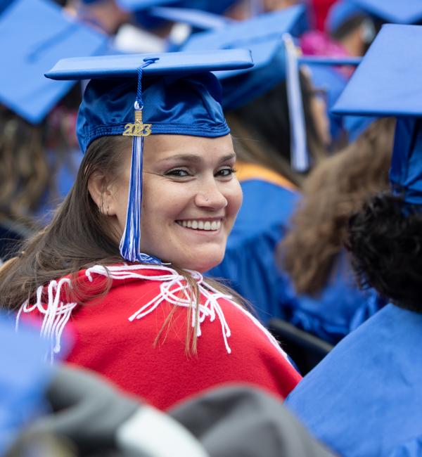 Student in a crowd smiling at camera in graduation cap and gown