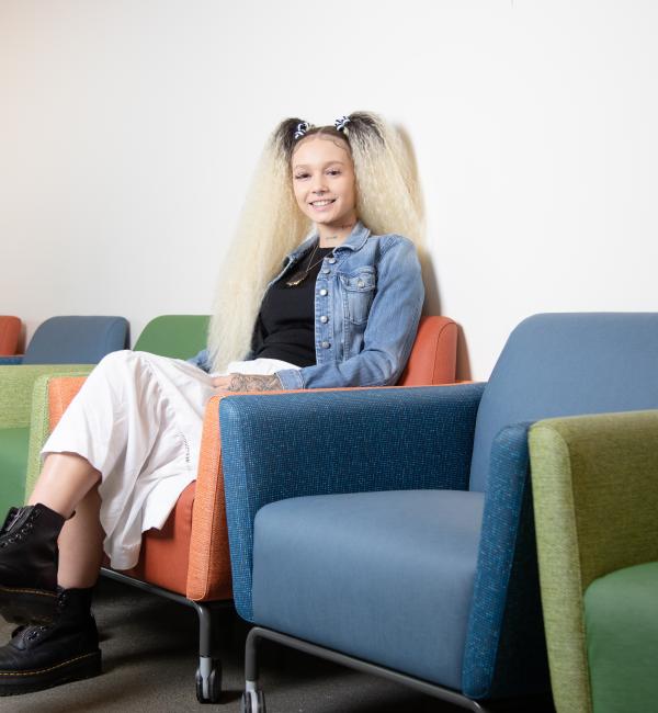 student sits in a row of colorful chair, smiling