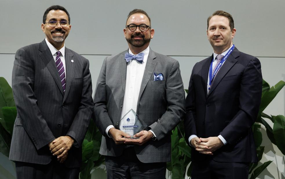 Dr. Stokes (center) holds glass award flanked by the two Aspen Prize co-Chairs