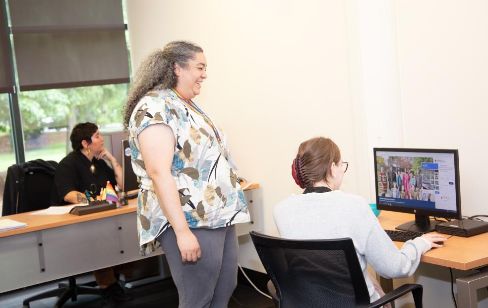staff member smiles while helping a student at a computer