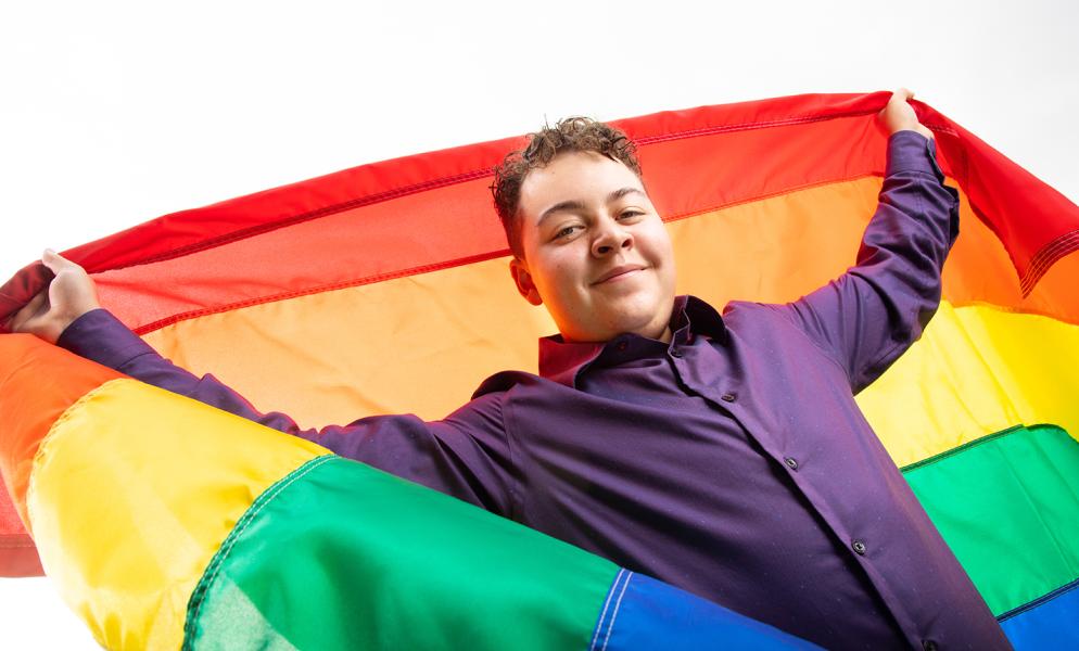 Student in a purple button up shirt holding a pride flag