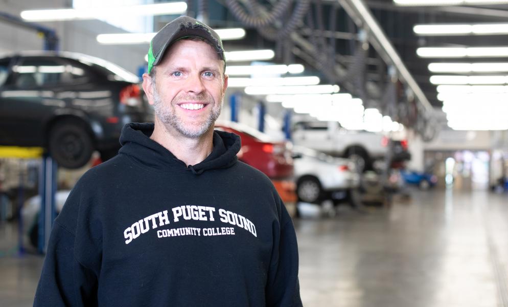 Tom Seal standing in SPSCC's automotive shop with cars on lifts in the background
