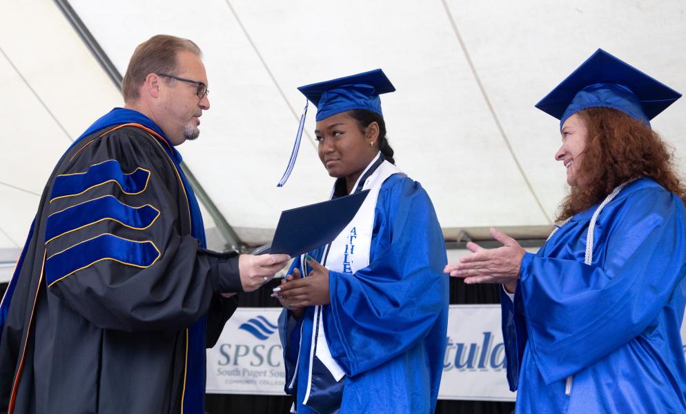 Two students dress in graduation caps and gowns receive an award from an SPSCC staff member.