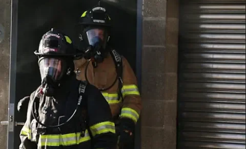 Two firefighters in fire hazard outfits standing in front of building